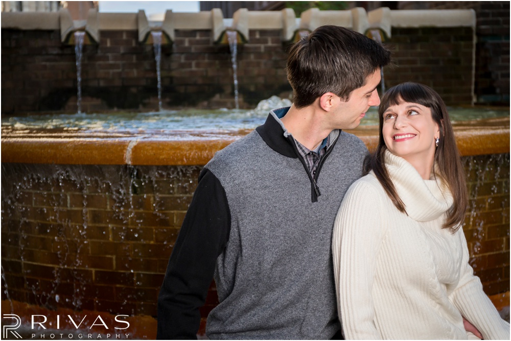 Timeless Garment District Engagement Session | A photo of an engaged couple in fall sweaters sitting by a fountain in Kansas City's Garment District. 