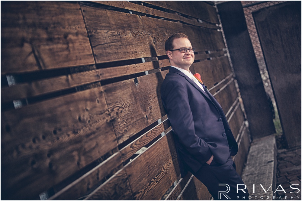Rustic Outdoor Fall Wedding | A picture of a groom leaning against a wooden plank wall on his wedding day. 