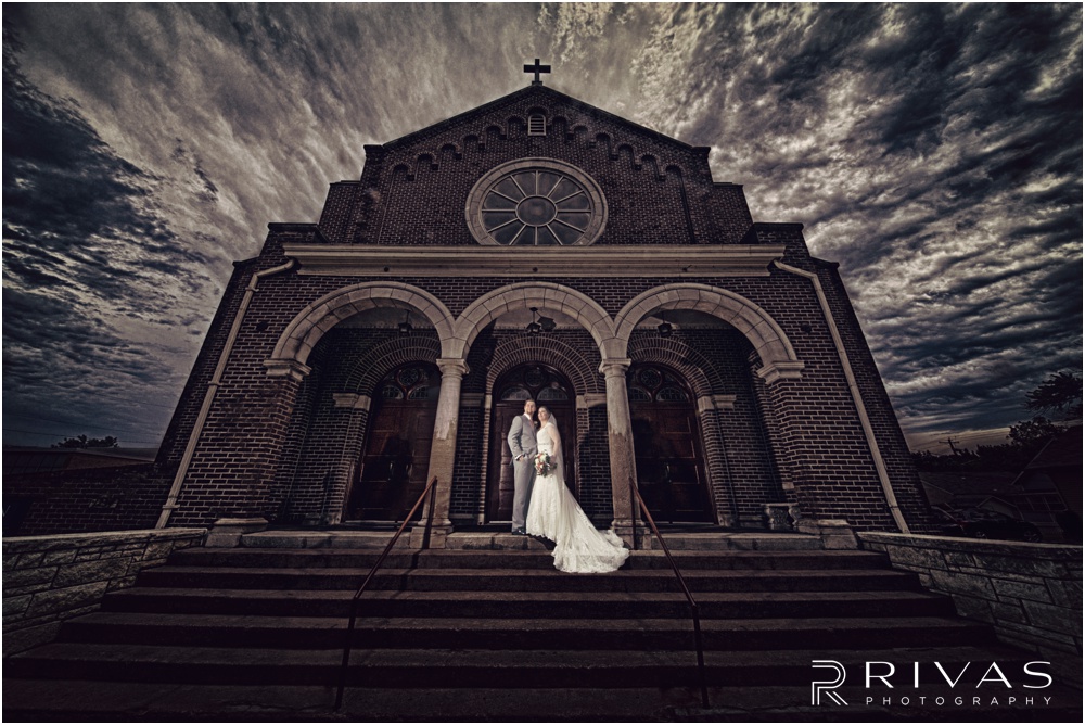 Lawrence KS Wedding Sneak Peek | A dramatic photo of a bride and groom standing on the steps of St. John the Evangelist Catholic Church in Lawrence KS. 