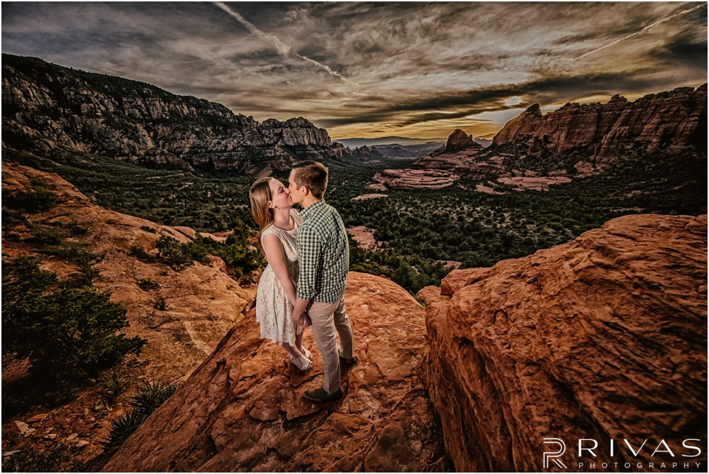 Merry-Go-Round Rock Engagement Session | Picture of an engaged couple kissing standing on a cliff at Merry-Go-Round Rock in Sedona. 