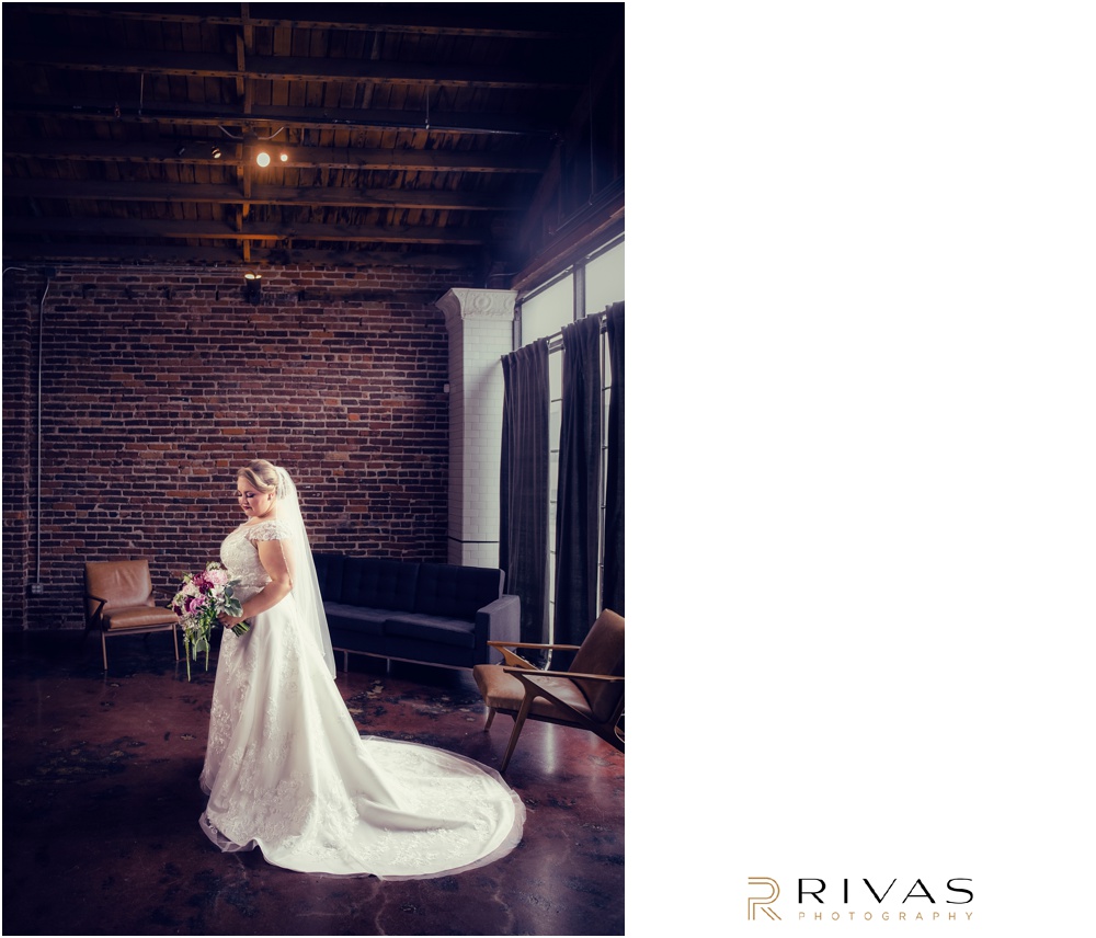 Vibrant Spring Wedding at The Guild | A portrait of a bride looking at her spring bouquet in her wedding gown in front of the brick wall at The Guild KC.  