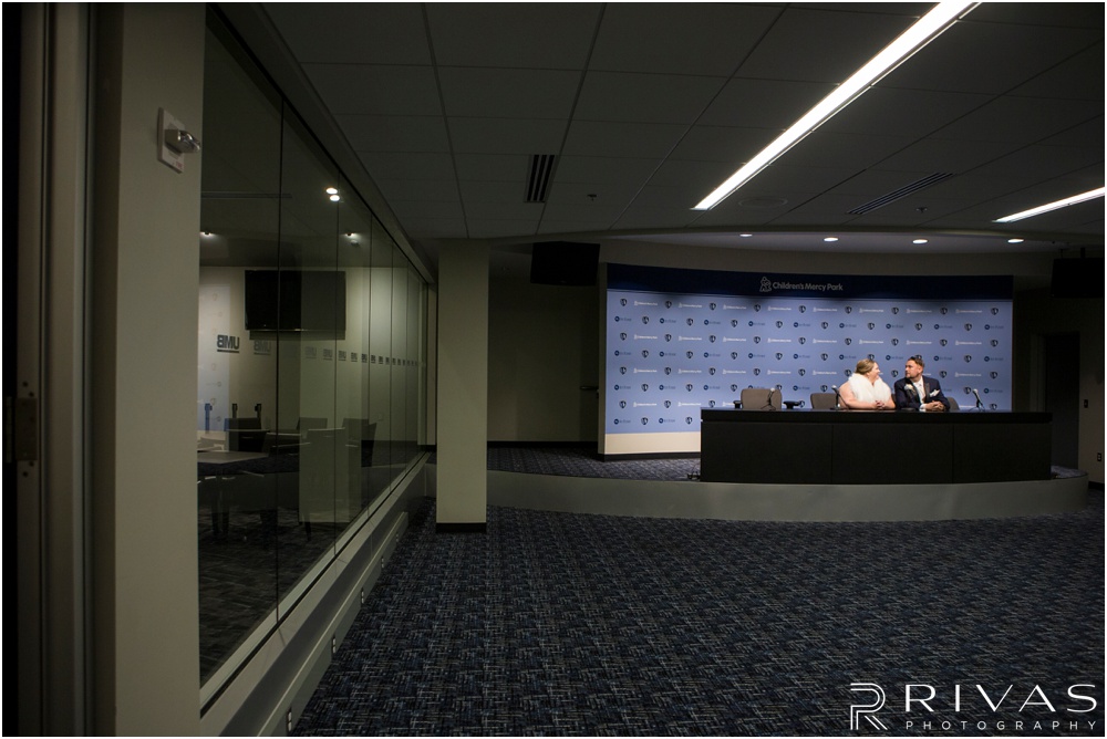 children's mercy park winter wedding | A picture of a bride and groom sitting at the interview desk in the media room of Children's Mercy Park. 