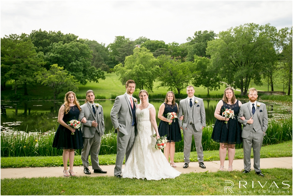 St. John the Evangelist Catholic Church Spring Wedding | A formal picture of a bride and groom with their wedding party standing in the grass in front of Potter Lake in Lawrence, KS. 