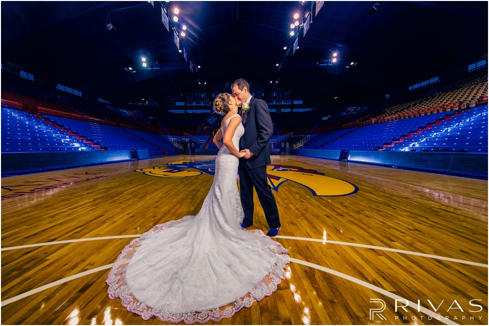 Allen Fieldhouse Wedding Pictures Sneak Peek | A dramatic portrait of a bride and groom sharing a kiss while standing just above the free-throw line on the court in Allen Fieldhouse. 
