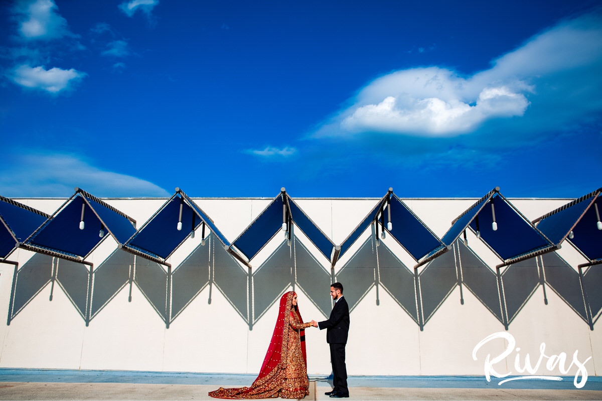 Westin Game Deck Bridal Session Sneak Peek | A formal portrait of an Indian bride and Iranian groom on their wedding day standing underneath a vibrant blue sky. 