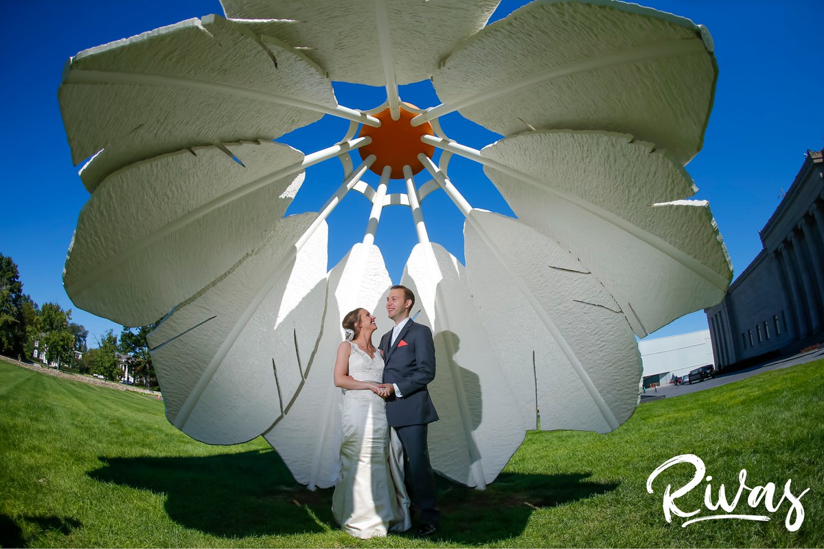 10 Years | A candid photo of a bride and groom on their wedding day sharing an embrace while standing underneath a shuttlecock sculpture at Kansas City's Nelson Atkins Museum of Art. 