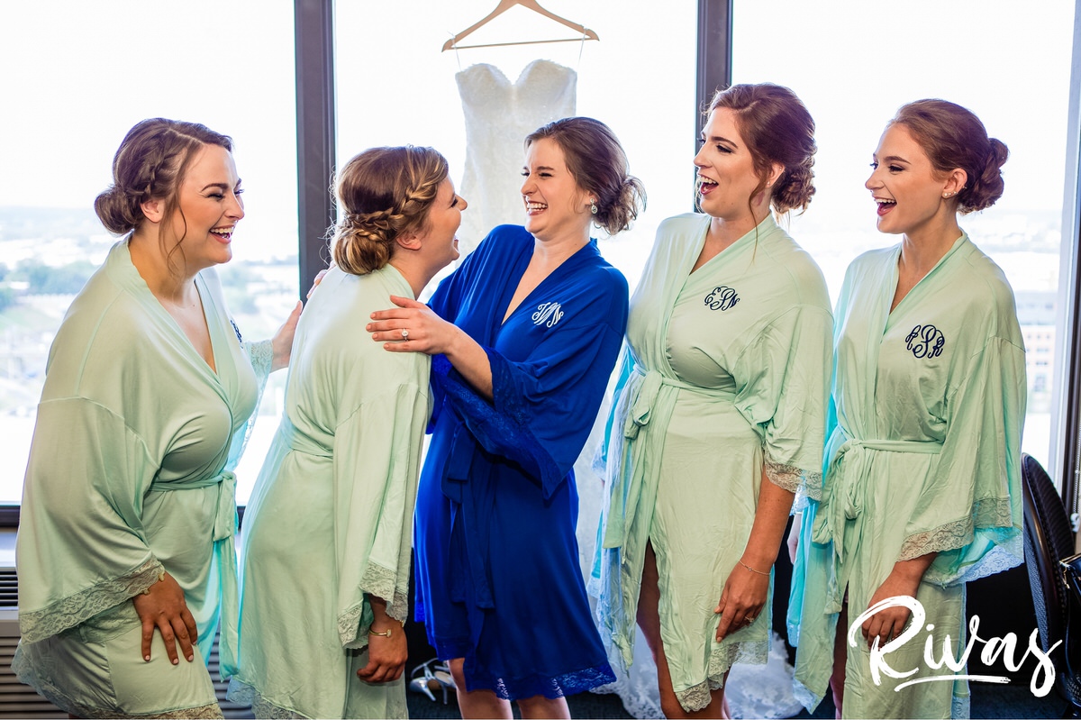 Strawberry Hill Summer Wedding | Rivas Photography | Kansas City Wedding Pictures | A candid image of a bride and her bridesmaids in coordinating robes embracing and laughing with each other on the morning of her wedding in Kansas City. 