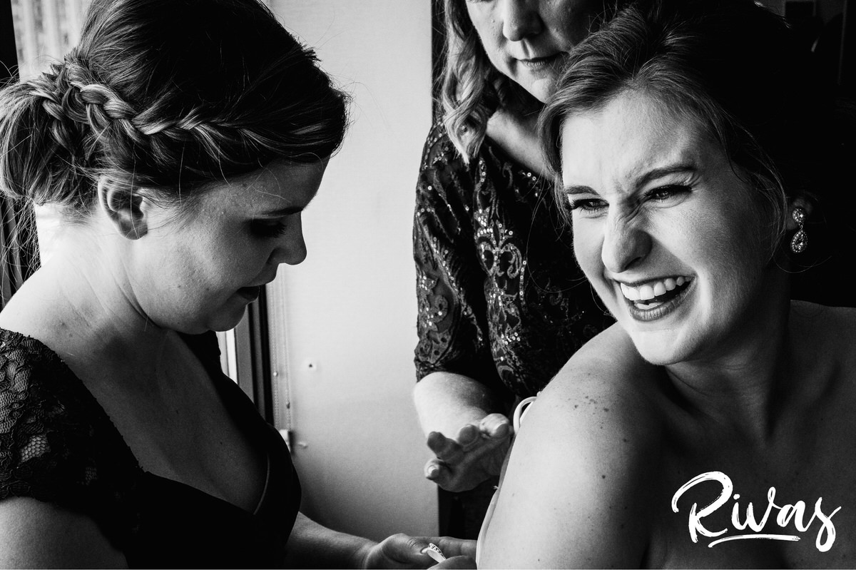 Strawberry Hill Summer Wedding | Rivas Photography | Kansas City Wedding Pictures | A close-up, candid black and white image of a bride laughing over her shoulder as her maid of honor and mother zip up the back of her wedding gown. 
