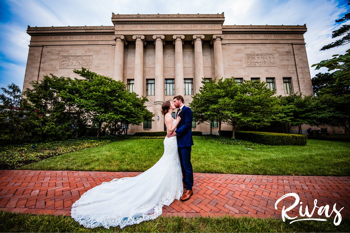 Strawberry Hill Summer Wedding | Rivas Photography | Kansas City Wedding Pictures | A vibrant photo of a bride and groom sharing an embrace as they stand on a path in front of the west side of the Nelson Atkins Museum of Art in Kansas City. 