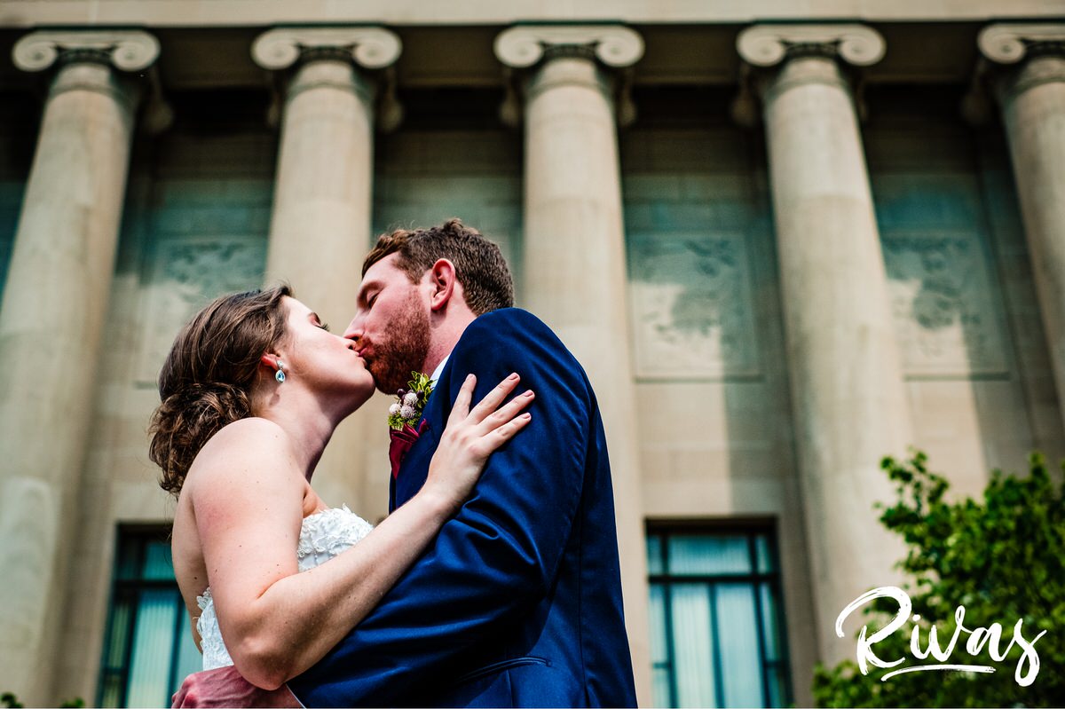 Strawberry Hill Summer Wedding | Rivas Photography | Kansas City Wedding Pictures | A picture taken from the ground looking up as a bride and groom share a kiss while standing in front of the columns at Kansas City's Nelson Atkins Museum of Art. 