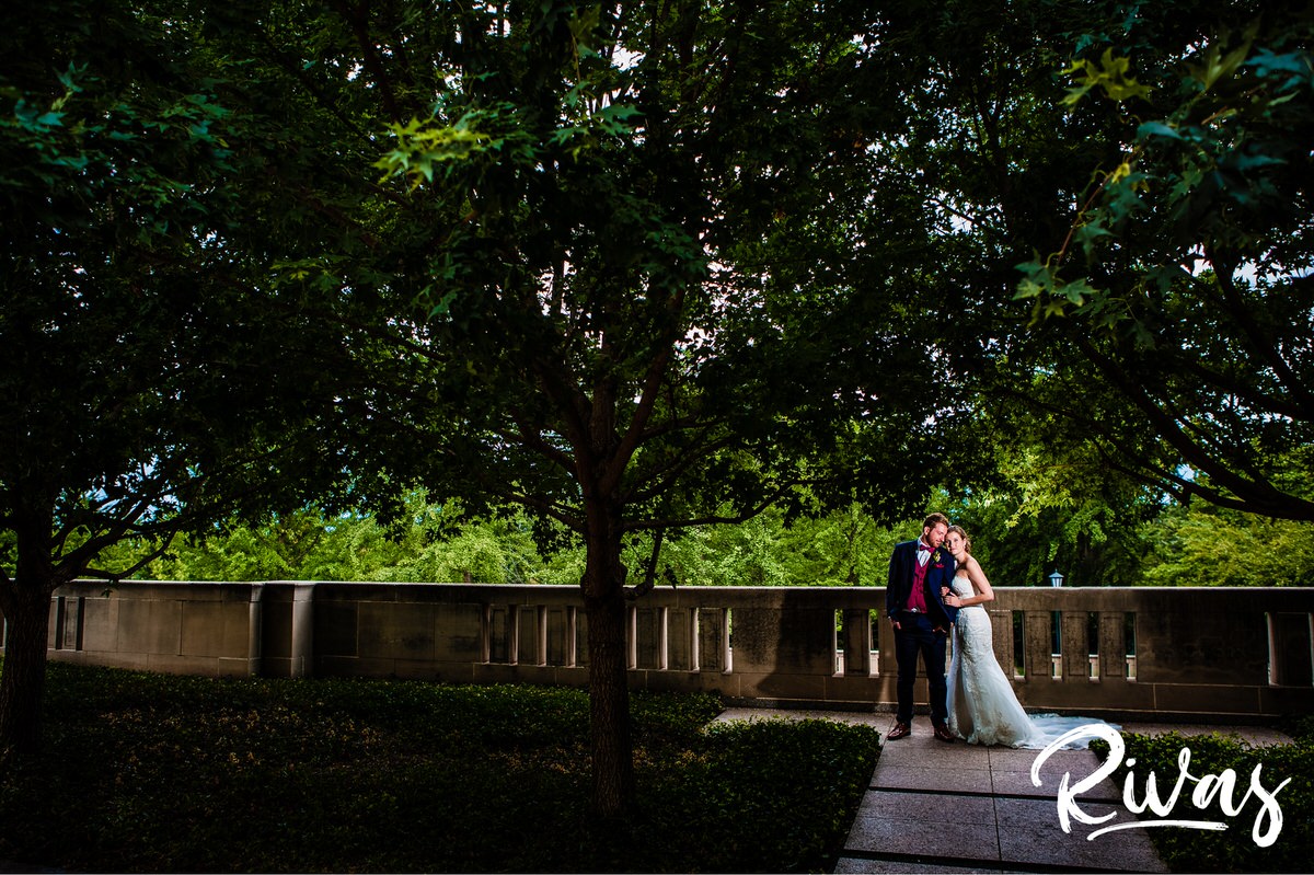 Strawberry Hill Summer Wedding | Rivas Photography | Kansas City Wedding Pictures | A dramatic photo of a bride and groom standing together underneath a canopy of green leaves at Kansas City's Nelson Atkins Museum of Art on their wedding day. 