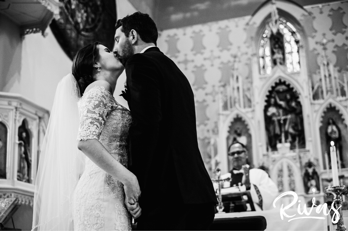Strawberry Hill Summer Wedding | Rivas Photography | Kansas City Wedding Pictures | A black and white, close-up picture of a bride and groom holding hands as they share their first kiss at the end of their wedding ceremony in Kansas City. 