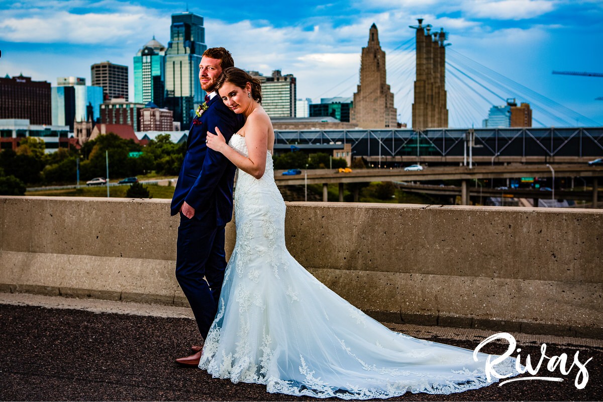 Strawberry Hill Summer Wedding | Rivas Photography | Kansas City Wedding Pictures | A candid picture of a bride standing behind her groom and resting her head on her shoulder overlooking the Kansas City skyline, taken from the Summit Street Bridge on their wedding day. 