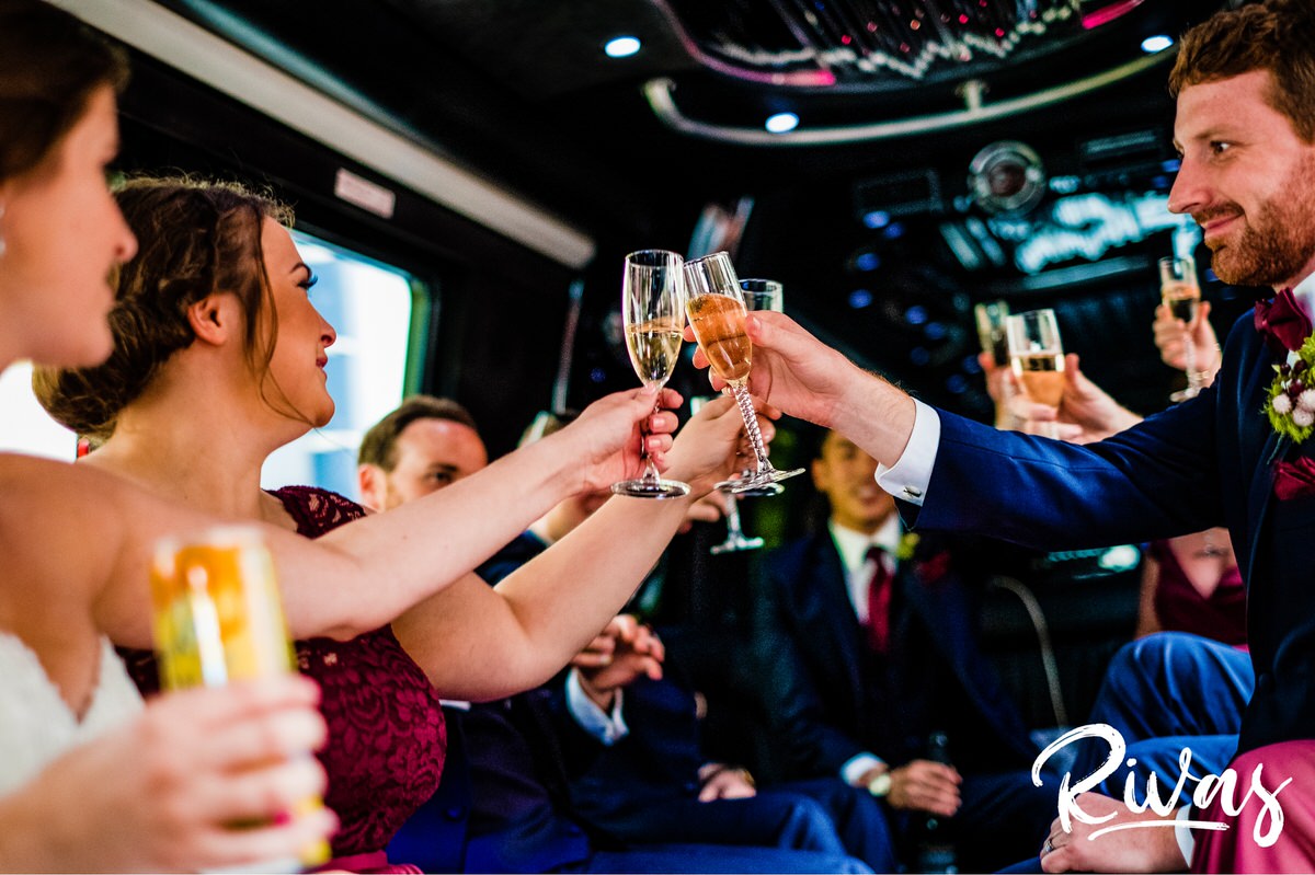 Strawberry Hill Summer Wedding | Rivas Photography | Kansas City Wedding Pictures | A candid photo on a party bus of a bride, groom, and their wedding party clinking full champagne glasses together as they ride around Kansas City on their wedding day. 