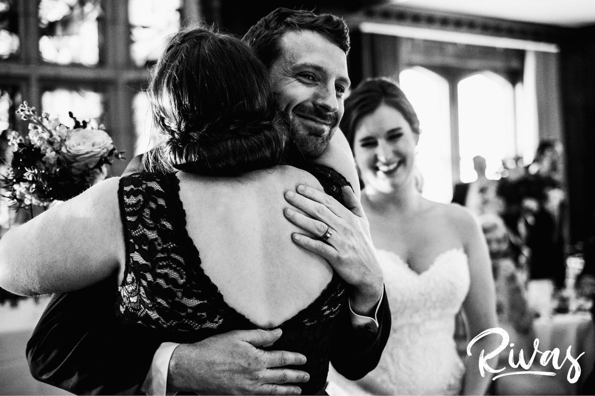 Strawberry Hill Summer Wedding | Rivas Photography | Kansas City Wedding Pictures | A black and white photo of a groom hugging a bridesmaid as his bride looks on during their wedding reception in The Tudor Room at Kansas City's Brass on Baltimore. 