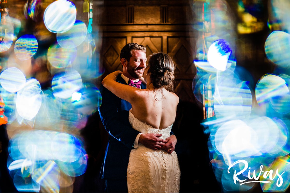 Strawberry Hill Summer Wedding | Rivas Photography | Kansas City Wedding Pictures | A vibrant photo taken through the gab between two champagne flutes of a bride and groom sharing their first dance during their wedding reception at The Tudor Room of The Brass on Baltimore in downtown Kansas City. 