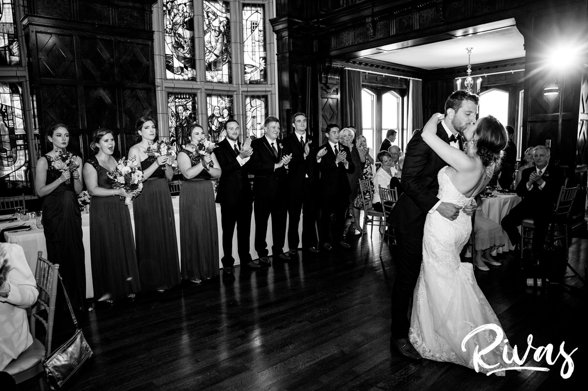 Strawberry Hill Summer Wedding | Rivas Photography | Kansas City Wedding Pictures | A wide, black and white image of a bride and groom sharing a kiss during the first dance of their wedding reception at Kansas City's Brass on Baltimore as their wedding party looks on. 