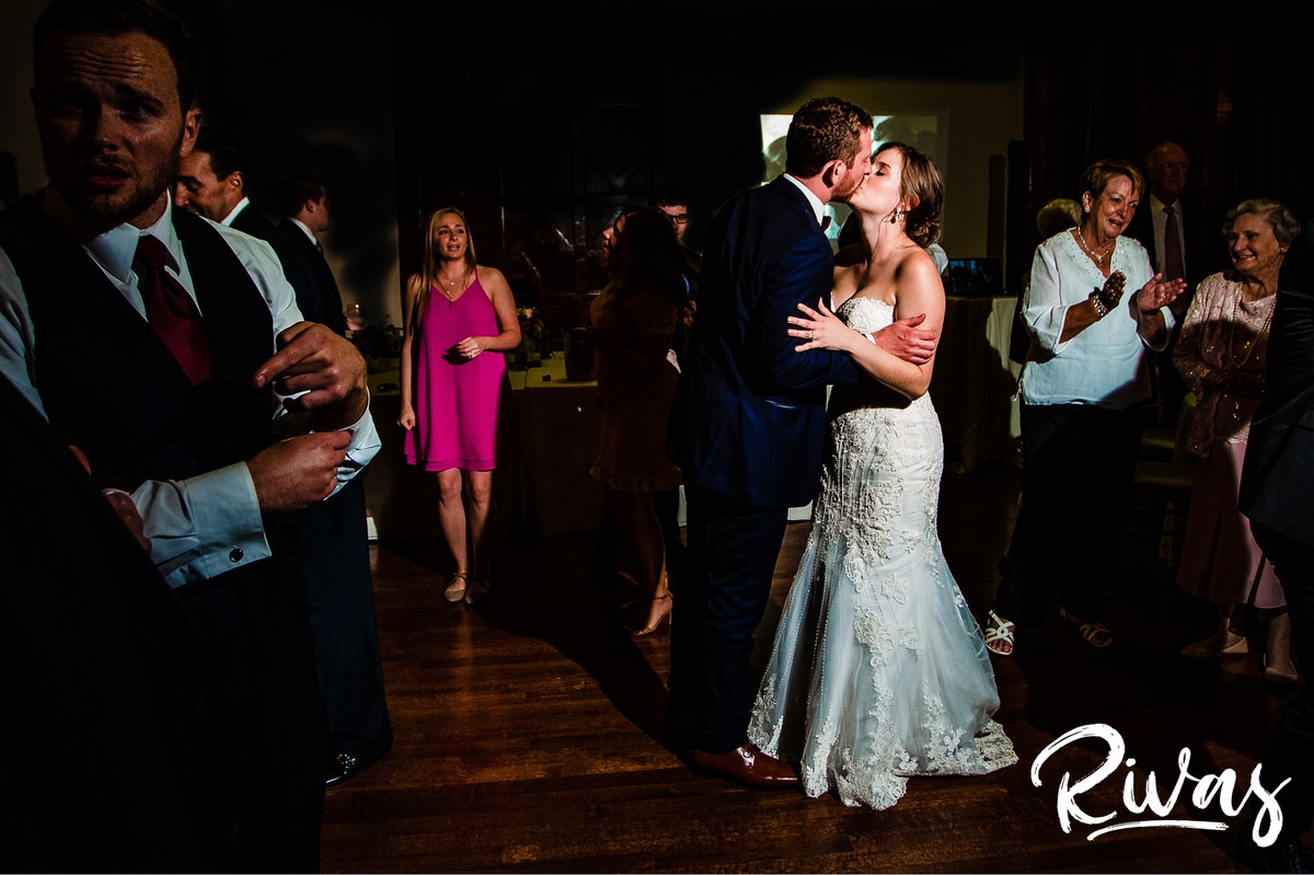 Strawberry Hill Summer Wedding | Rivas Photography | Kansas City Wedding Pictures | A candid picture of a bride and groom sharing a kiss while standing on the dance floor surrounded by family and friends during their wedding reception in The Tudor Room at Kansas City's Brass on Baltimore. 