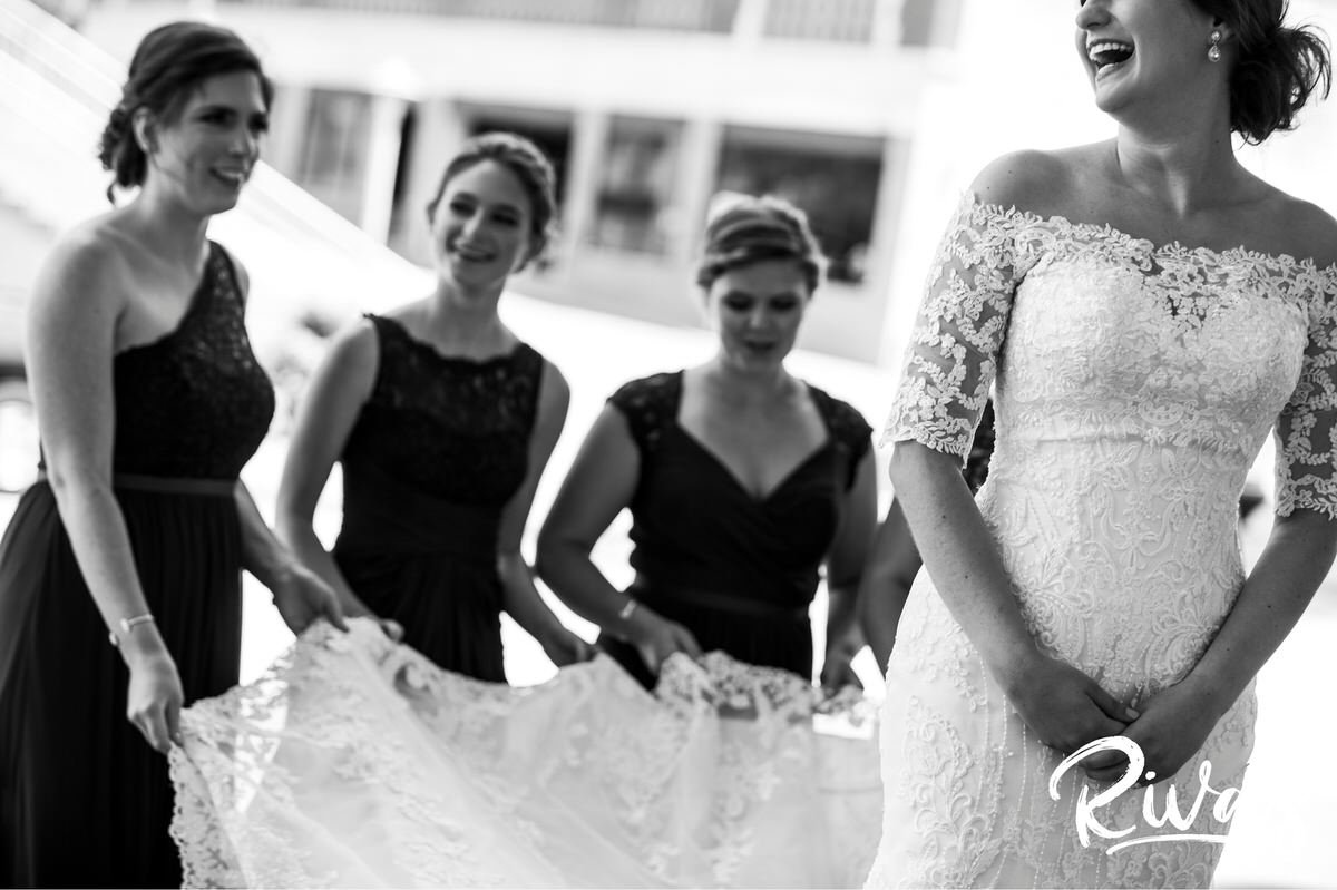 Strawberry Hill Summer Wedding | Rivas Photography | Kansas City Wedding Pictures | A black and white candid picture of a bride's bridesmaids carrying the train of her gown across the street in downtown Kansas City on the morning of her wedding. 
