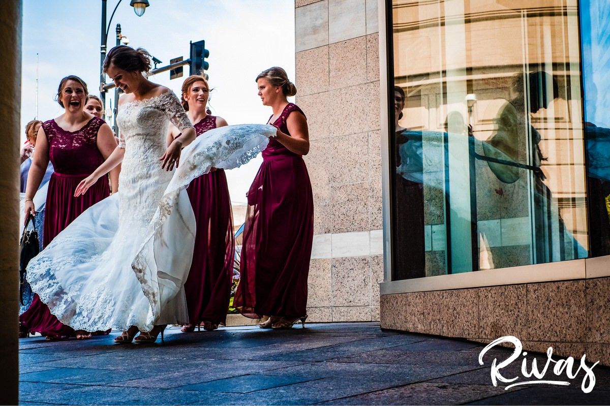 Strawberry Hill Summer Wedding | Rivas Photography | Kansas City Wedding Pictures | A candid picture of a group of bridesmaids dressed in long burgundy gowns holding a bride's train as it blows in the wind. 