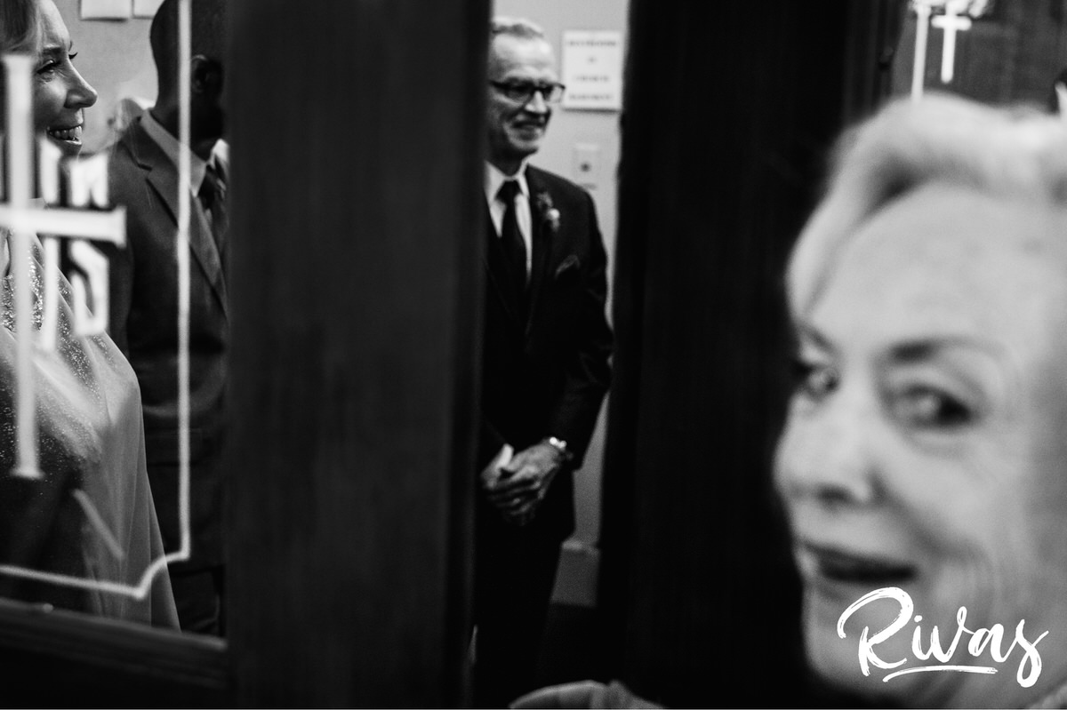 Strawberry Hill Summer Wedding | Rivas Photography | Kansas City Wedding Pictures | A candid black and white picture of a groom's grandma looking out from a door that the groom, his mom, and the bride's father are standing just inside of on the morning of his wedding. 