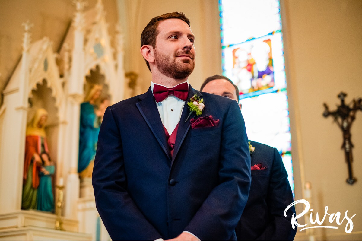Strawberry Hill Summer Wedding | Rivas Photography | Kansas City Wedding Pictures | A photo taken looking up of a groom dressed in a navy suit with maroon bow tie waiting at the front of the church for his bride to walk down the aisle. 