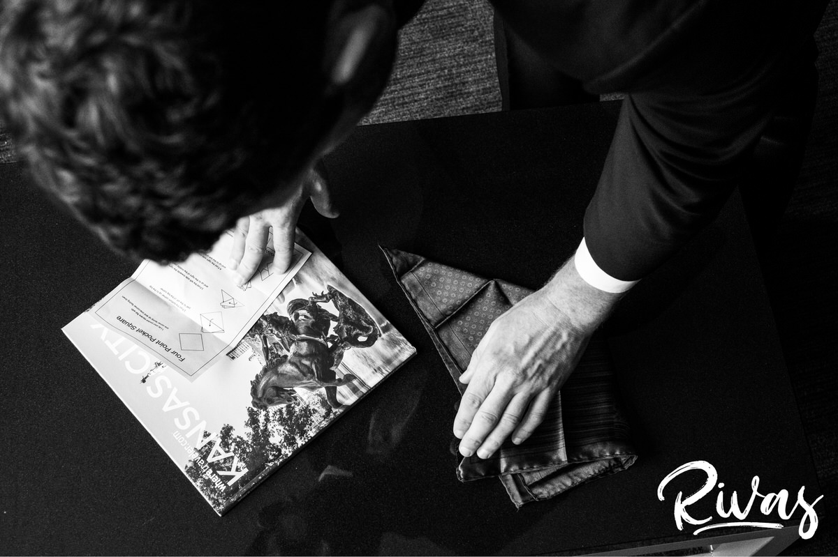 Strawberry Hill Summer Wedding | Rivas Photography | Kansas City Wedding Pictures | A black and white image taken from the top-down of a groom following detailed instructions on folding pocket squares on the morning of his Kansas city wedding. 
