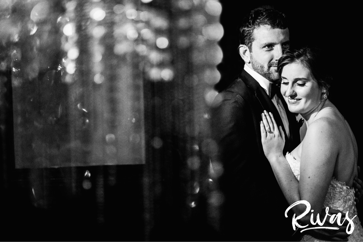 Strawberry Hill Summer Wedding | Rivas Photography | Kansas City Wedding Pictures | Two black and white vertical photos taken through the 6 story chandelier of a bride and groom sharing an embrace on their wedding day at Kansas City's Brass on Baltimore. 