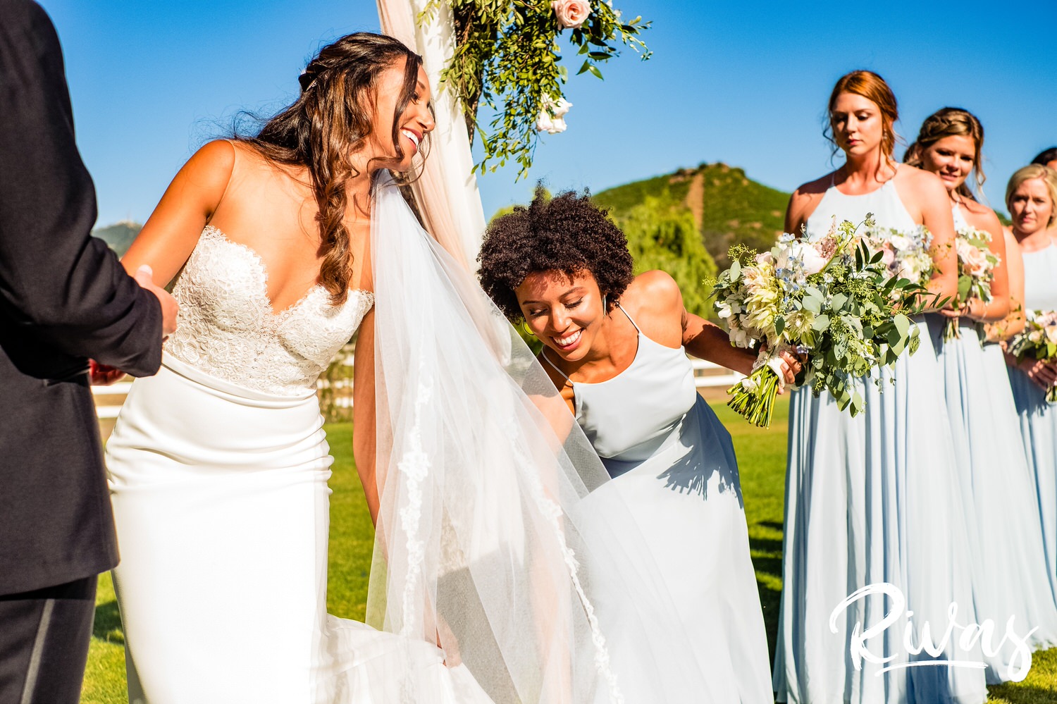 Saddlerock Ranch Summer Wedding | Destination Wedding Photographers | Rivas | A candid picture of the maid of honor adjusting the bride's train and veil at the altar. 