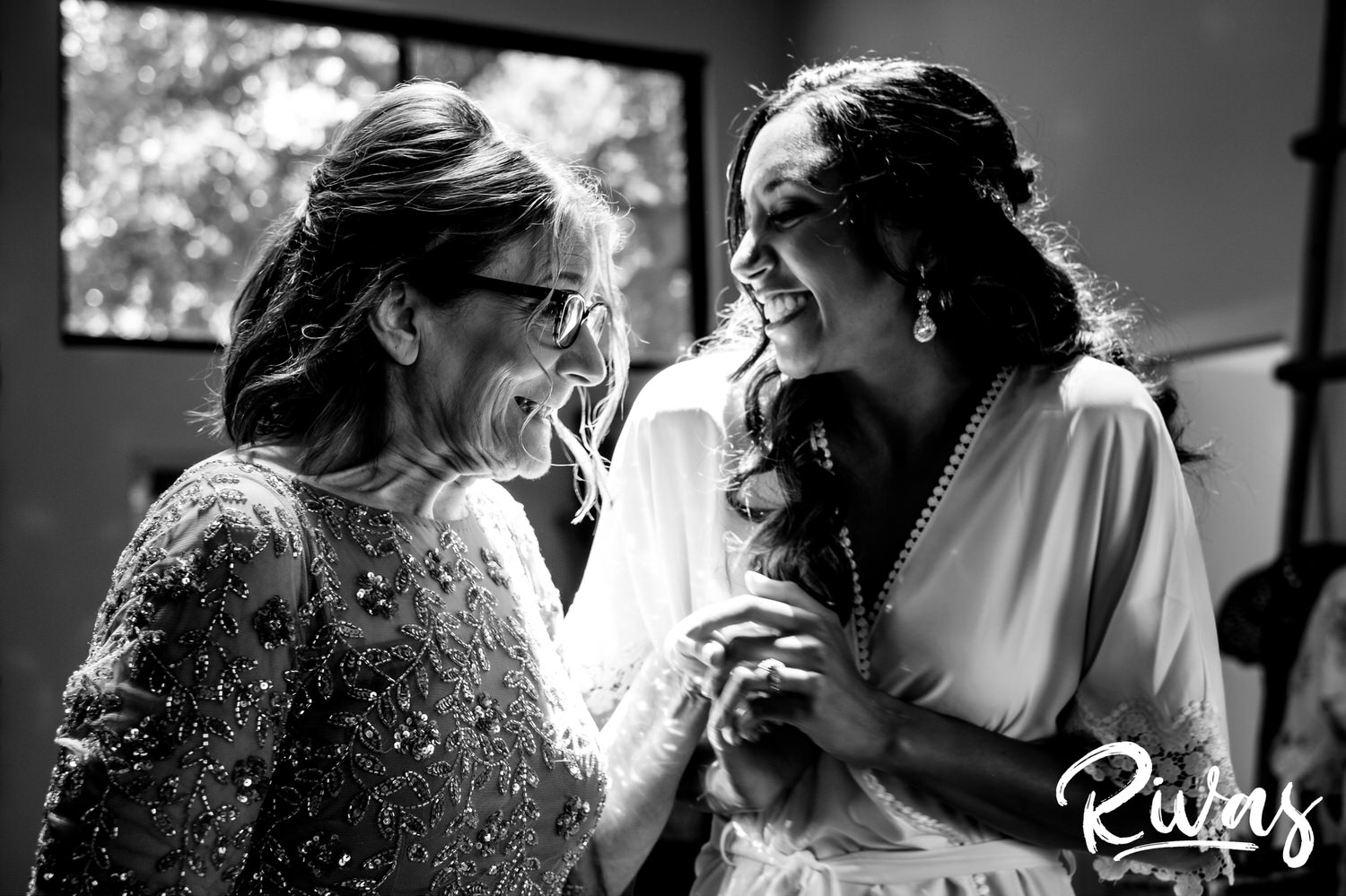 Saddlerock Ranch Summer Wedding | Destination Wedding Photographers | Rivas | A black and white picture of a bride and her mom holding hands and grinning at each other just before the bride puts on her wedding gown. 