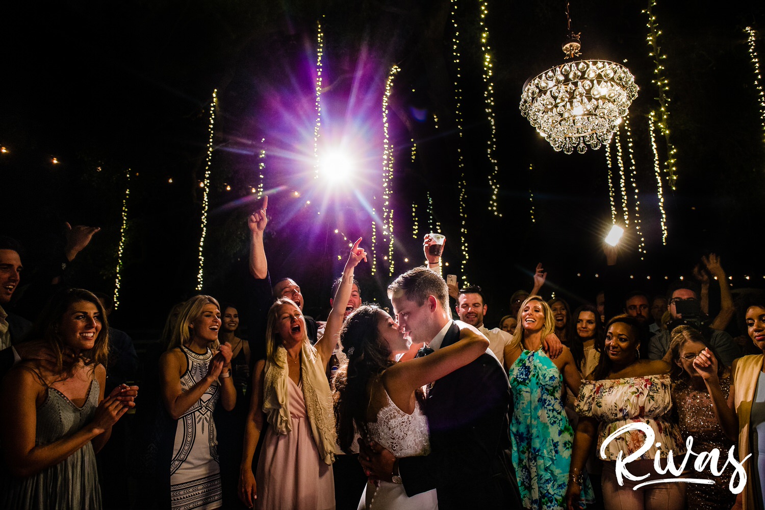 Saddlerock Ranch Summer Wedding | Destination Wedding Photographers | Rivas | A candid image of a bride and groom dancing under a chandelier and ropes of twinkly lights while their friends and family cheer them on during their wedding reception at Saddlerock Ranch in Malibu, CA. 