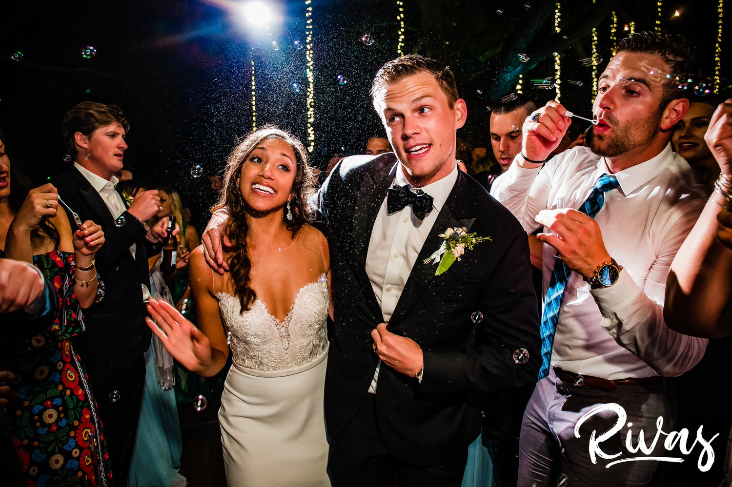 Saddlerock Ranch Summer Wedding | Destination Wedding Photographers | Rivas  | A photo of a bride and groom singing and exiting their wedding under a sea of bubbles and ropes of twinkly lights at Malibu's Saddlerock Ranch. 
