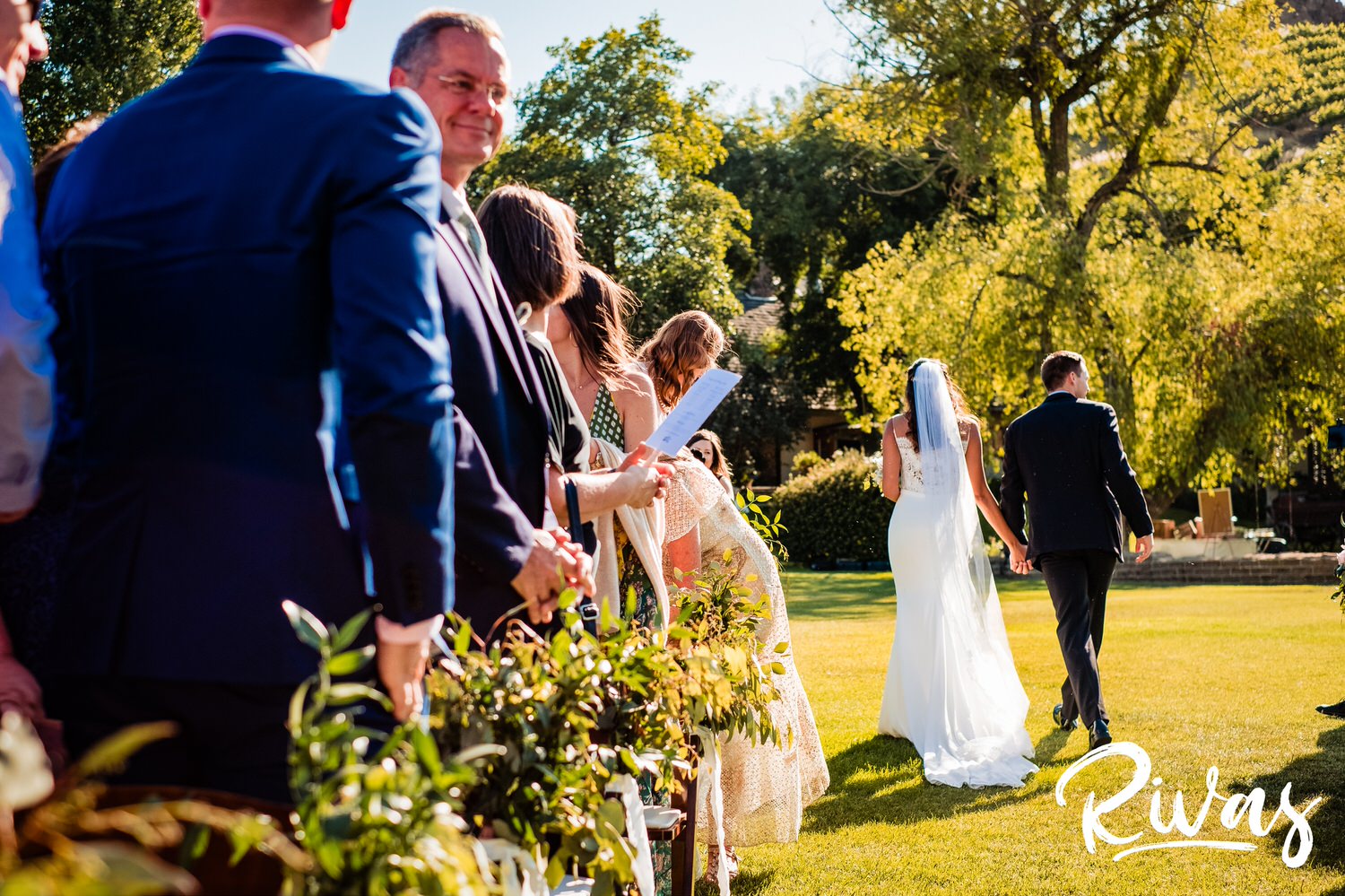 Saddlerock Ranch Summer Wedding | Destination Wedding Photographers | Rivas | A candid photo of the bride and groom walking back down the aisle holding hands, taken from their viewpoint. 
