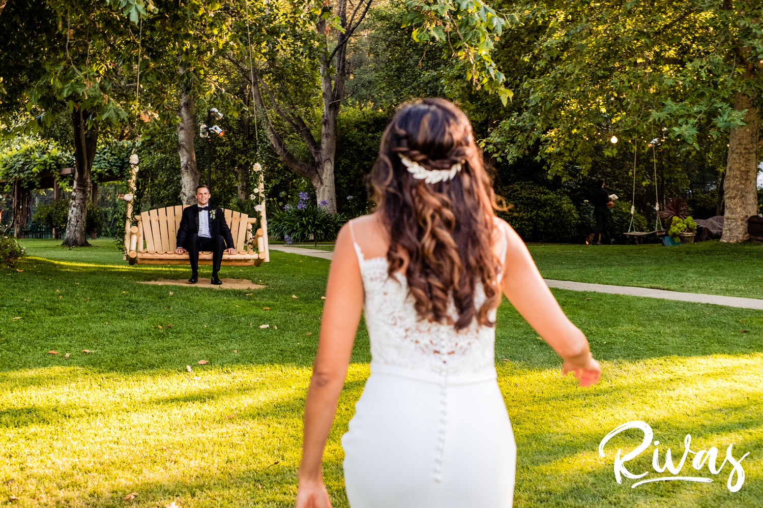 Saddlerock Ranch Summer Wedding | Destination Wedding Photographers | Rivas | A candid photo of a bride walking towards her groom who is sitting on a wooden swing hung from the trees. 