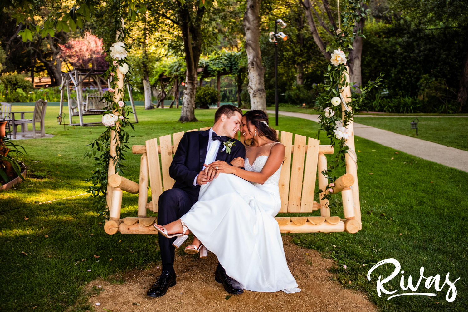 Saddlerock Ranch Summer Wedding | Destination Wedding Photographers | Rivas | An image of a bride and groom snuggling while sitting on a wooden swing hung from the trees. 