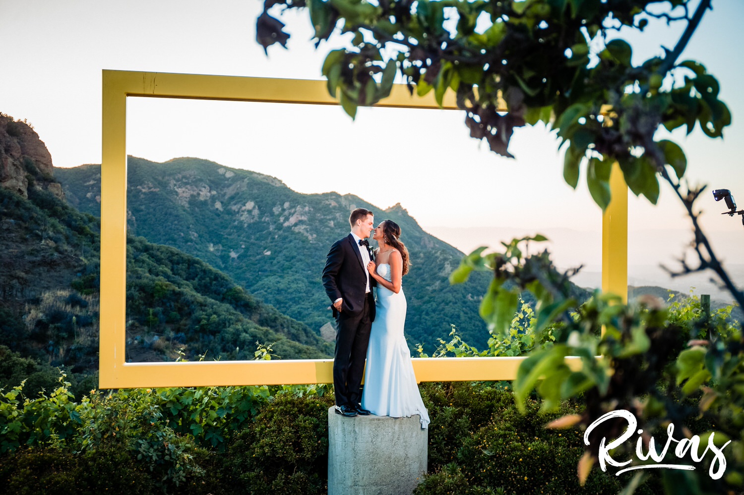 Saddlerock Ranch Summer Wedding | Destination Wedding Photographers | Rivas | A photo of a bride and groom sharing an embrace on their wedding day in front of the iconic yellow frame at Saddlerock Ranch in Malibu, California. 