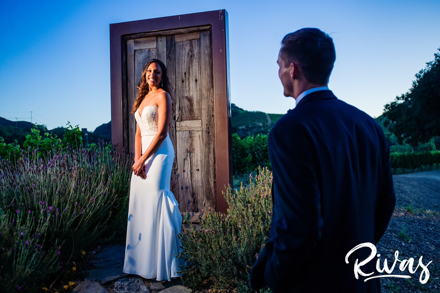 Saddlerock Ranch Summer Wedding | Destination Wedding Photographers | Rivas | A photo of a bride and groom with the bride turned and smiling back at the groom while standing in front of the "door to anywhere" at Malibu's Saddlerock Ranch. 