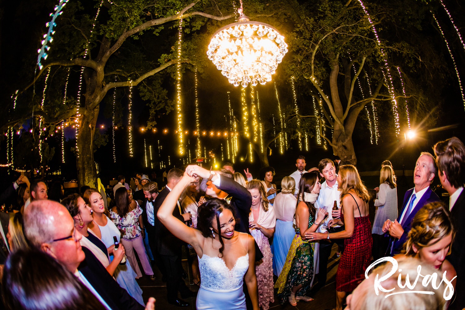 Saddlerock Ranch Summer Wedding | Destination Wedding Photographers | Rivas | A picture of a groom twirling his bride underneath his arm as they dance outside underneath a chandelier and ropes of twinkly lights during their Saddlerock Ranch Wedding Reception in Malibu, California. 