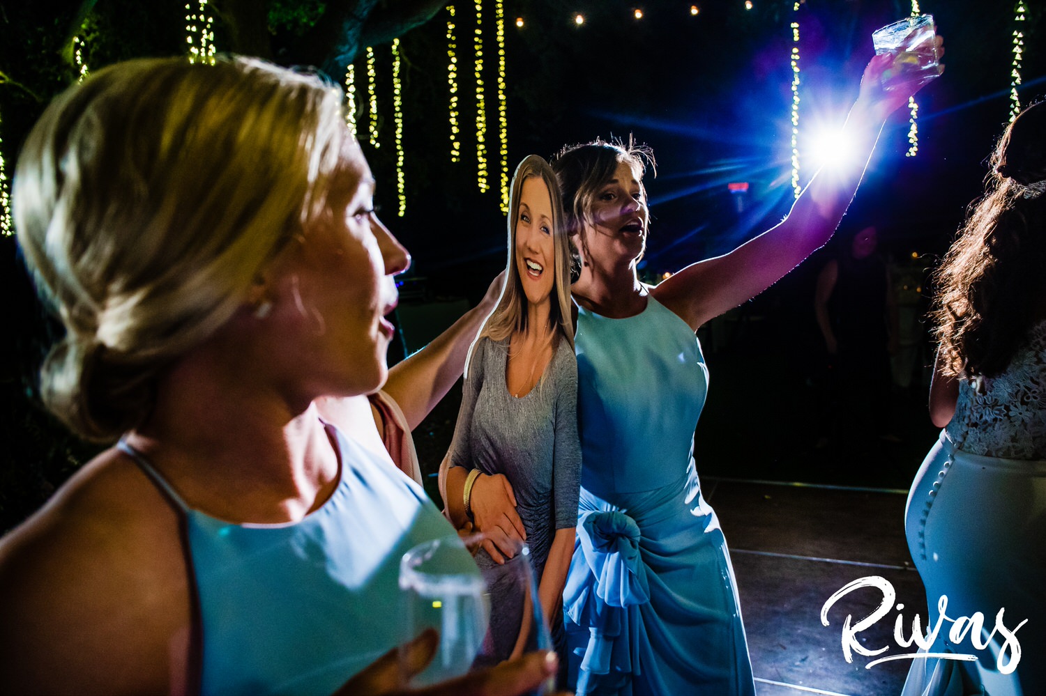 Saddlerock Ranch Summer Wedding | Destination Wedding Photographers | Rivas | A photo of two bridesmaids dressed in blue holding drink glasses and dancing with a life size cutout of a pregnant bridesmaid on the dance floor of a wedding reception at Saddlerock Ranch in Malibu, California. 