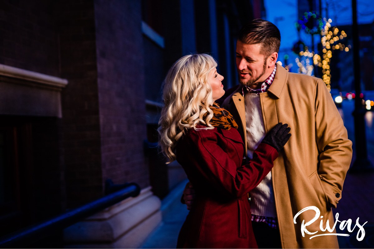 KC Winter Lights Engagement Pictures | Kansas City engagement Pictures | Rivas | A picture taken through a strand of white Christmas lights of an engaged couple laughing together during their winter engagement session in Kansas City. 