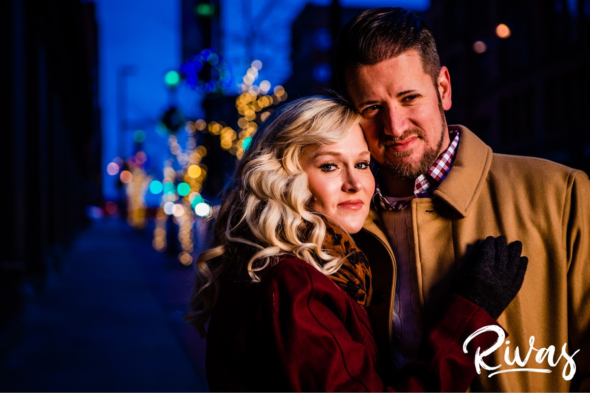KC Winter Lights Engagement Pictures | Kansas City engagement Pictures | Rivas | Two images of an engaged couple sharing an embrace as they walk down a city street and pause underneath a lit streetlight to share a kiss during their winter engagement session in Kansas City. 