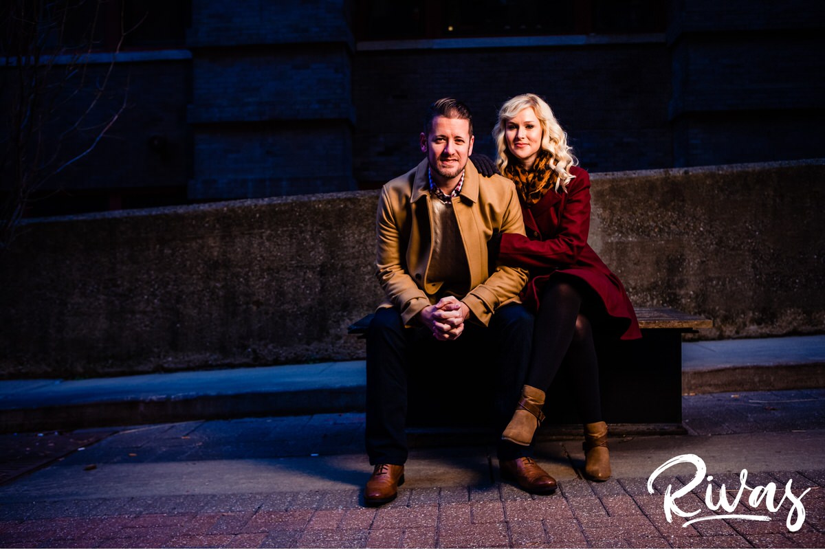 KC Winter Lights Engagement Pictures | Kansas City engagement Pictures | Rivas | A picture of an engaged couple in dressy coats sitting on a bench, sharing an embrace and snuggling in during their winter engagement session. 