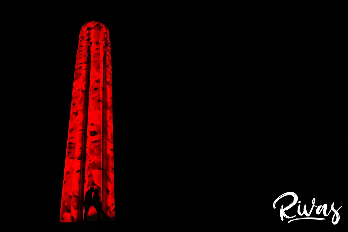 Nighttime Liberty Memorial Engagement Sneak Peek | KC Wedding Photographers | Rivas | A silhouetted portrait of an engaged couple sharing an embrace in front of the pipe at Liberty Memorial, lit up with poppies in remembrance and celebration of the Armistice Centennial Event in Kansas City.  