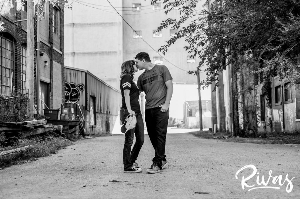 West Bottoms Engagement Pictures | A black and white picture of an engaged couple walking down an alley holding hands and sharing a kiss. 