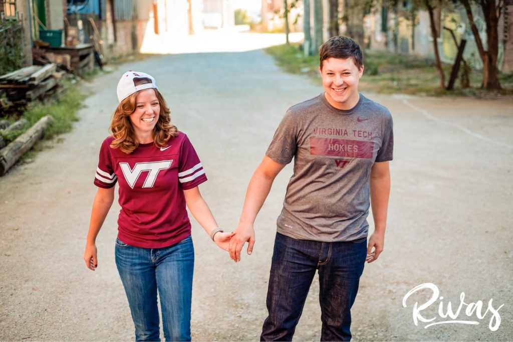 West Bottoms Engagement Pictures | a picture of a couple dressed in Virginia Tech gear holding hands and laughing together in Kansas City's West Bottoms neighborhood. 