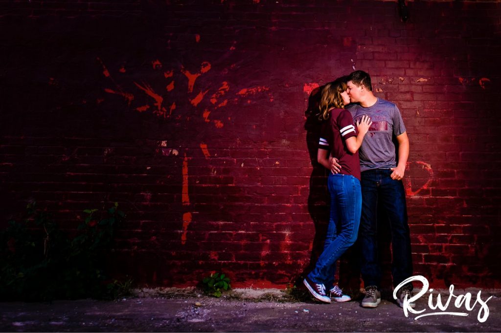 West Bottoms Engagement Pictures | A picture of an engaged couple in Virginia Tech gear standing up against a red brick wall. 