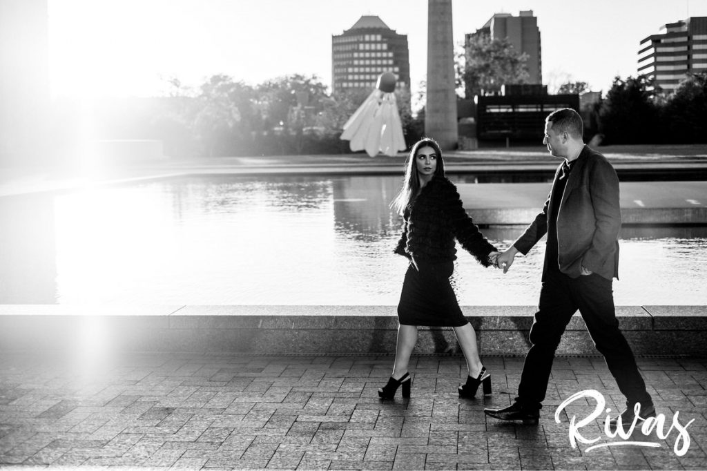 A dramatic, black and white picture of an engaged couple holding hands and walking in front of the reflecting pool at the Nelson during their colorful Nelson engagement session. 