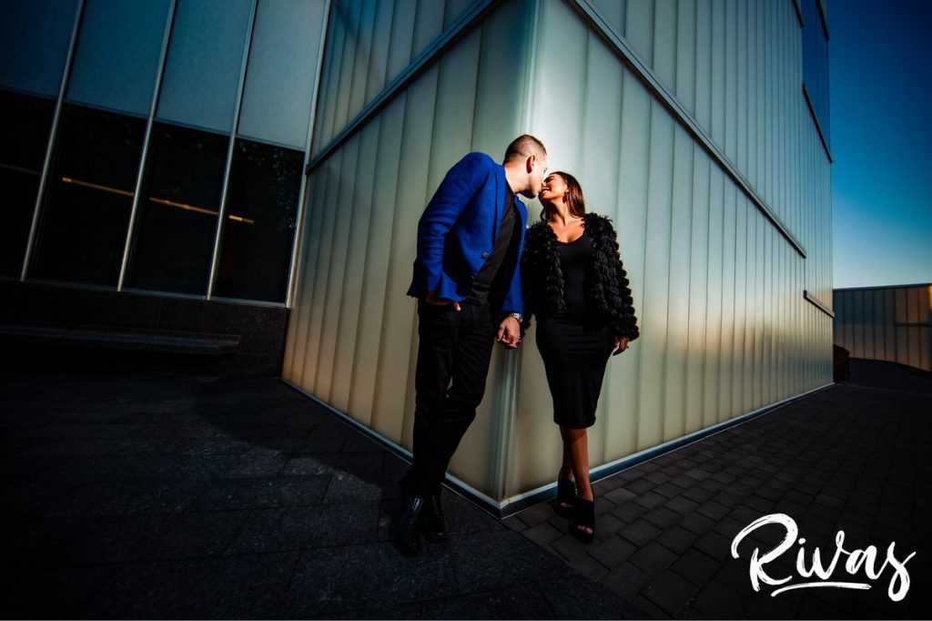 A colorful picture of an engaged couple holding hands and reaching around the corner as they stand against two sides of The Nelson's Bloch Building during their colorful Nelson Engagement Session. 