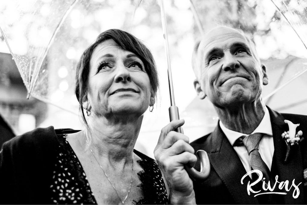 Art Deco Inspired Wedding in Kansas City | A close-up picture of a bride's parents holding a clear umbrella over their heads as they watch their daughter get married. 