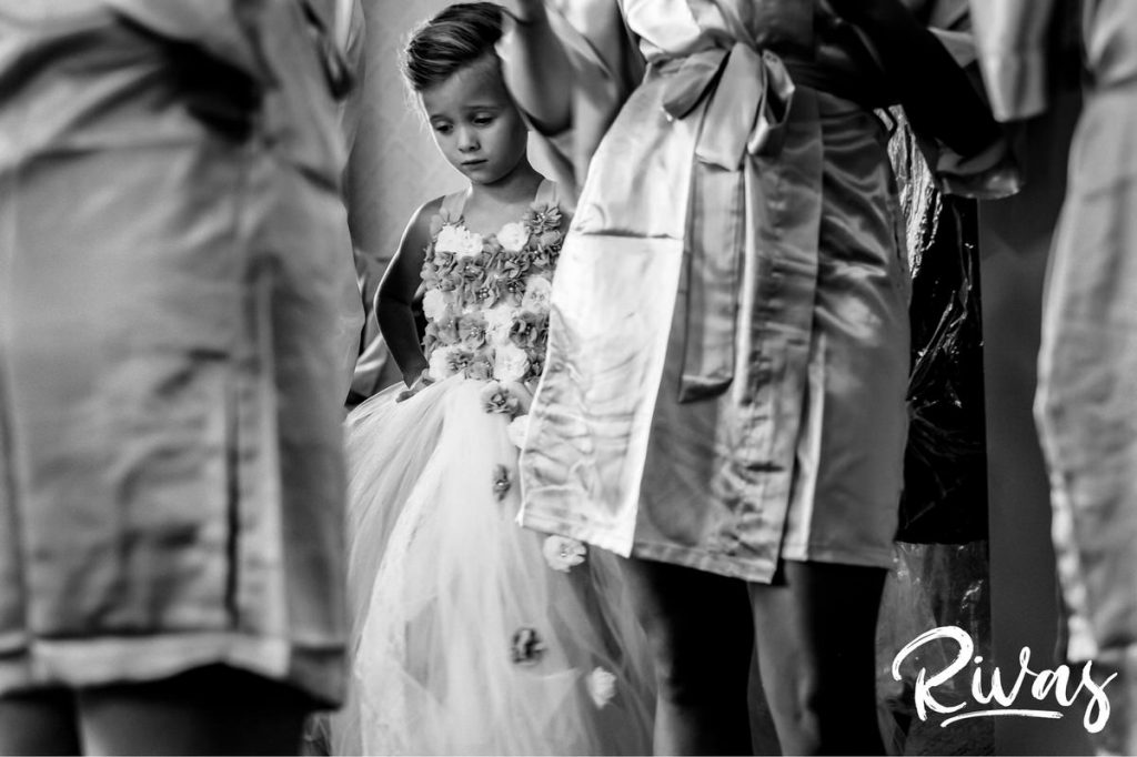 Art Deco Inspired Wedding in Kansas City | A candid black and white picture of a flower girl sadly looking down as she stands with a group of bridesmaids in matching robes. 